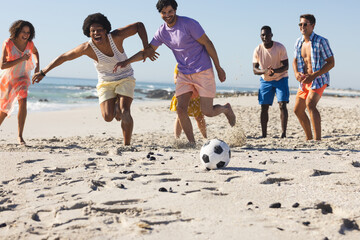 Diverse group of friends play soccer on the beach