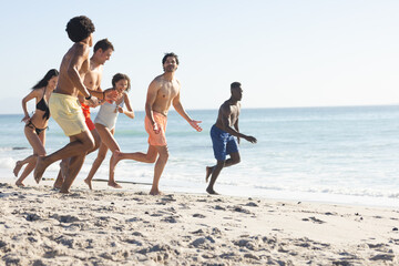 Diverse friends enjoy a lively race on a sunny beach, with copy space