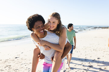 Young African American man gives a piggyback ride to a Caucasian woman on the beach