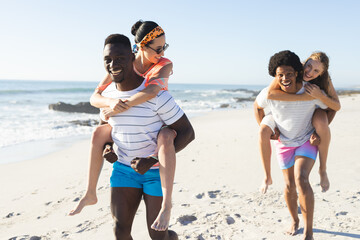 Diverse friends enjoy piggyback rides on a sunny beach