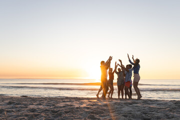 Diverse friends celebrate on the beach at sunset, with copy space