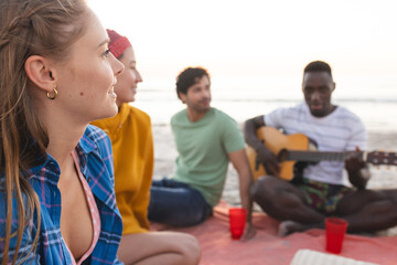 Diverse friends enjoy a beach gathering at sunset, having a party