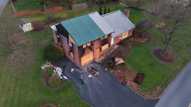Aerial view of a damaged brick house with a tarped roof and debris scattered on the driveway. Significant fire insurance claim, American home.