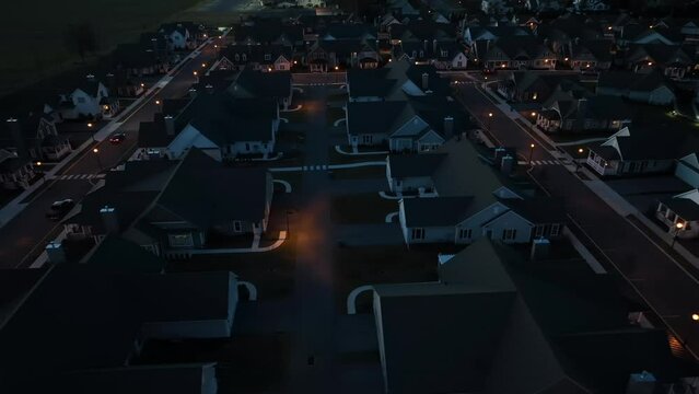 Aerial truck shot of dark neighborhood at night. Development with town lights in background. High view at dusk with car headlights.