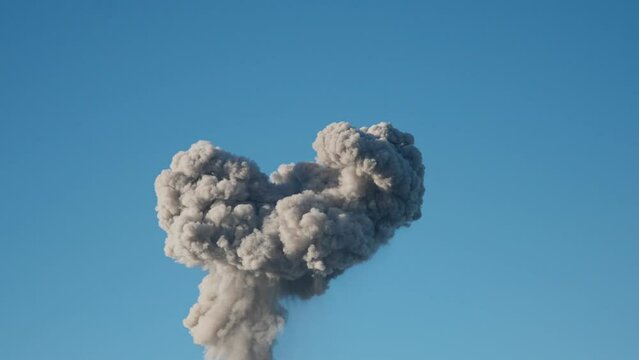 Explosion causes mushroom cloud to rises into blue sky in war zone