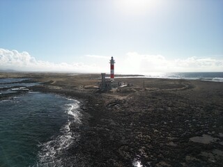 The 19th century red and white bands Faro del Tostón lighthouse located on the northwest coast of Fuerteventura in the Canary Islands. A lighthouse against the background of the blue sky and the ocean