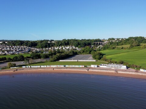 Aerial photo of Goodrington Sands Beach in Paignton Torbay showing the shoreline and a long row of beach huts with blue sea and sky on a sunny morning.