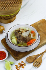 Sop daging sapi or Indonesian beef soup, served on ceramic white bowl with sambal and slices of lime. Selective focus with white marble background. 