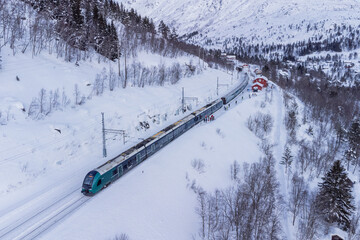 Tran on the famous Bergen - Oslo line is standing on the first track at Mjolfjell train station in the middle of the route. Snow and winter capped mountains around, also the next track is in snow.
