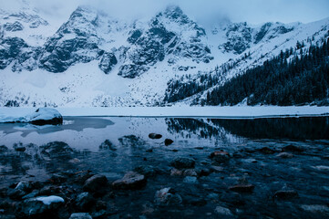 A freezing Morskie Oko lake nestled in a natural landscape of snowcovered mountains and trees,...