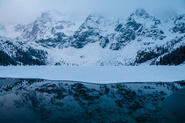 An atmospheric natural landscape with a Morskie Oko lake reflecting snowcovered mountains, creating...
