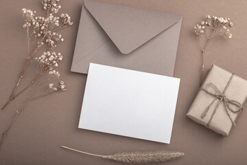 Beige envelope on a beige background, gift box and dried gypsophila flowers. Warm earthy tones. Postcard.