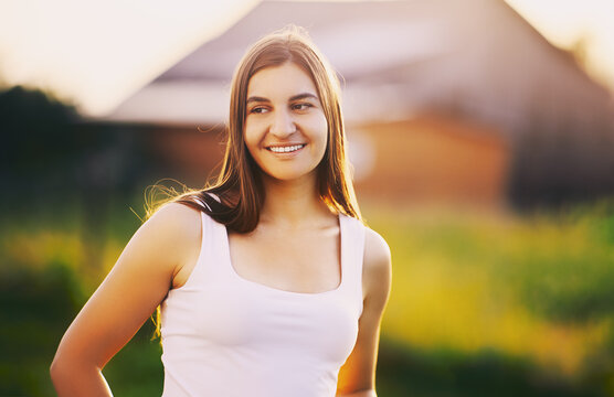 Perfect smile of young Caucasian woman with perfect teeth at setting sun against blurred background of rural landscape.