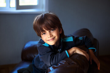 Happy preschooler boy on brown leather sofa in darkened room.