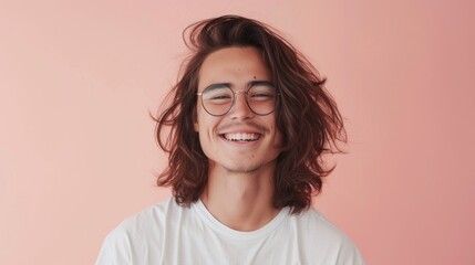 Obraz premium A young man with long hair wearing glasses smiling at the camera against a pink background.