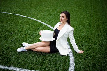 A business woman with a large cup, sitting on a green lawn in the park.