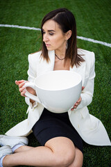 A business woman with a large cup, sitting on a green lawn in the park.