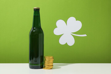Green bottle, gold coins and clover leaf on green background, space for text