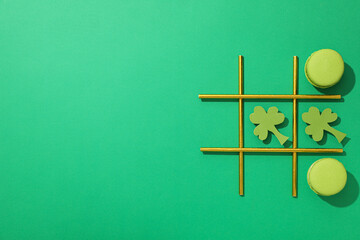Paper clover leaves, macaroons, and cocktail straws on green background, space for text
