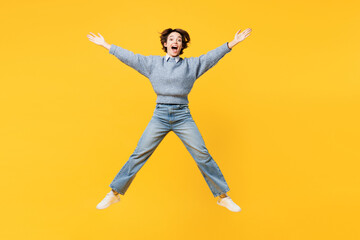 Fototapeta na wymiar Full body astonished fun young woman she wears grey knitted sweater shirt casual clothes jump high with outstretched hands arms isolated on plain yellow background studio portrait. Lifestyle concept.