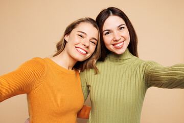 Close up fun young friends two women they wear orange green shirt casual clothes together doing selfie shot pov on mobile cell phone isolated on plain pastel light beige background. Lifestyle concept.