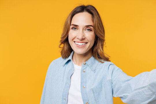 Close up young smiling happy woman she wear blue shirt white t-shirt casual clothes doing selfie shot pov on mobile cell phone isolated on plain yellow background studio portrait. Lifestyle concept.