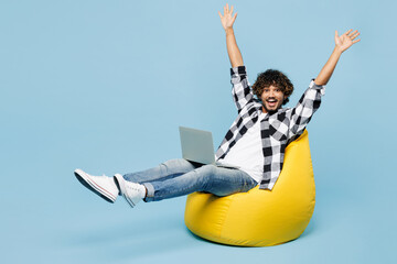Full body young Indian IT man he wears shirt white t-shirt casual clothes sit in bag chair hold use...