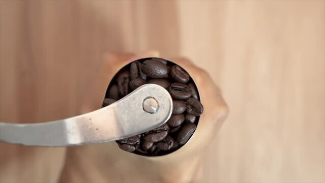 slow motion of preparing to grind coffee beans by hand Put coffee beans into a stainless steel hand grinder, top view.