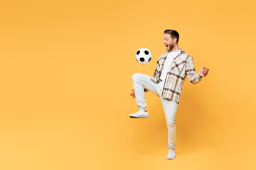 Full body young fun man fan wear brown shirt casual clothes cheer up support football sport team hold juggling soccer ball watch tv live stream look aside on area isolated on plain yellow background