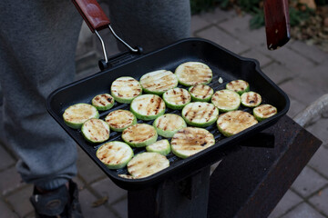 Grilling courgette slices, prepare warm camp  food outdoors. Zucchini cut cooking on black grill pan. Contrast light round vegetable slices baked for family dinner without oil. Healthy vegetarian food