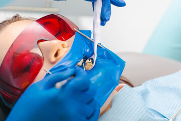 Close up shot of a female patient at the dentist wearing latex dental dam and protection glasses. - obrazy, fototapety, plakaty