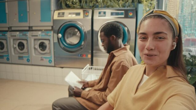 POV UGC footage of positive Caucasian lady in hairband recording video for vlog and talking about taking self-service in public laundry