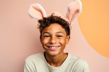 
Photography an indigenous boy, aged 15, smiling warmly with bunny ears on his head, against a gentle pastel peach backdrop, ideal for Easter-themed advertisements or social media posts - obrazy, fototapety, plakaty