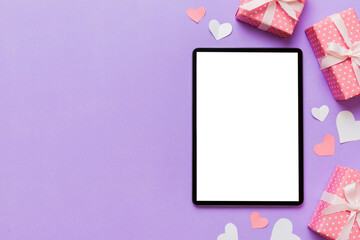 Top view of digital tablet with gift boxes and hearts on colorful background. Tablet with black screen with Holiday decorations gift box top view