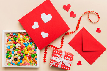 Red envelope with candy and gift box and Valentines hearts on colored background. Flat lay, top view. Romantic love letter for Holiday concept