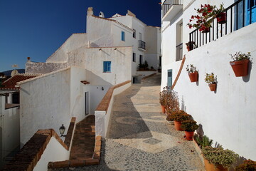 Picturesque narrow and steep cobbled alleys in Frigiliana, Axarquia, Malaga province, Andalusia, Spain, with traditional whitewashed little houses and decorated with colorful flowers and plants
