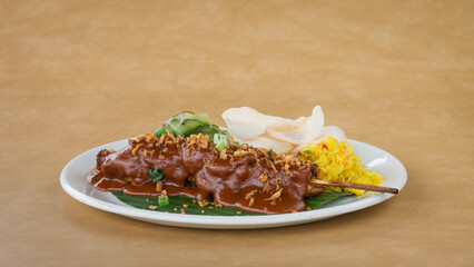 Chicken covered with Satay sauce, prawn crackers and garnish on white plate with light brown background