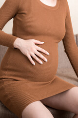 Pregnant Lady Having Massaging Lower belly Sitting On Sofa Indoor. Pregnancy Problems Concept. Maternity healthcare