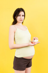 pregnant woman holding a bottle and a pile of pills in hands at colorful background with copy space. Healthcare concept