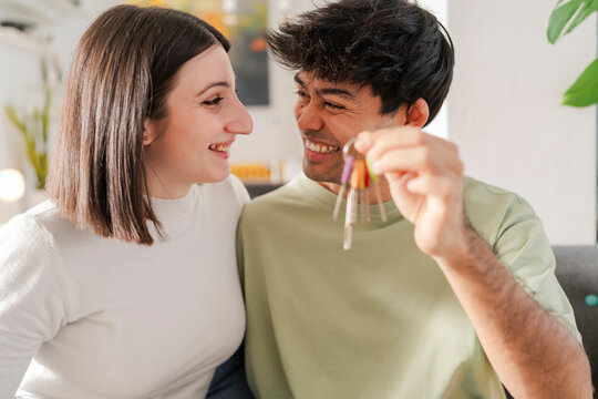 Smiling young couple excitedly holding a bunch of colorful keys, celebrating a new home ownership together