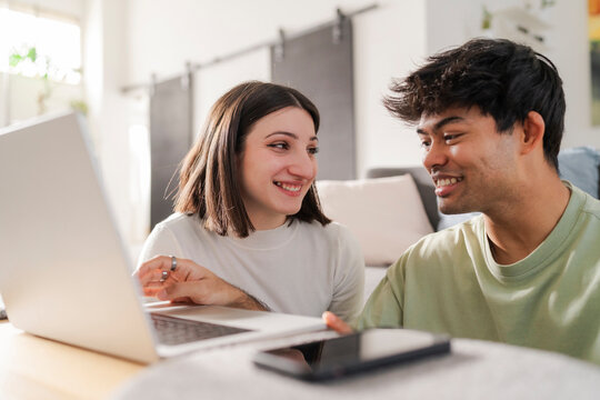 Young couple sharing a fun moment while shopping online, with the woman pointing at the laptop screen and smiling