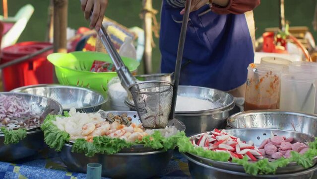 This engaging stock footage captures a Thai woman meticulously preparing ingredients to cook at the bustling floating market in Hat Yai, Thailand