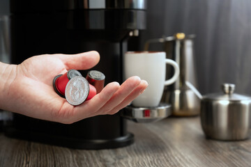 Close-up of a capsule for a coffee machine in a hand against the background of a kitchen.