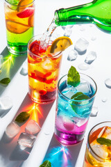 Drink poured from a bottle into transparent glasses, colourful cocktails at sunlight with shadow and reflections. Summer refreshment beverage.