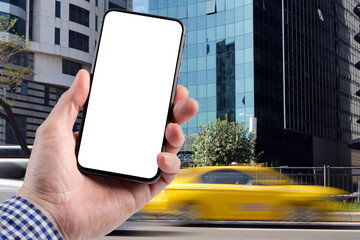 A man holds a smartphone in his hand on a background yellow taxi drive quickly along the road in...