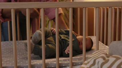 Cropped shot of unrecognizable caring mother putting adorable little baby boy to sleep in soft cozy crib