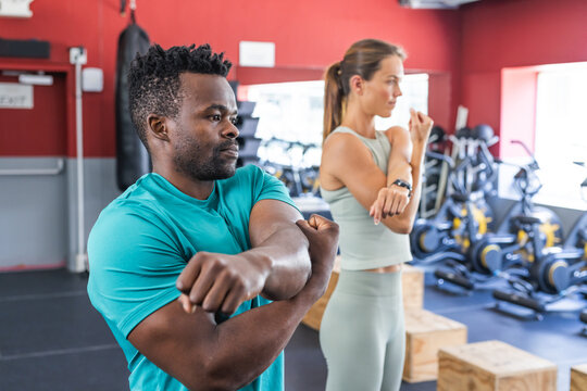 Fit African American man and young Caucasian woman stretching at the gym
