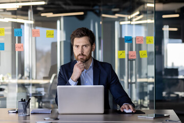 Focused mature businessman at his desk in a bright office, contemplating with sticky notes...