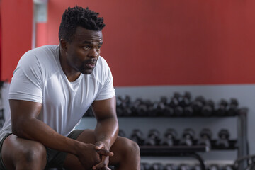 A fit African American man rests during a gym workout