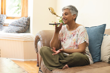 A mature biracial woman speaks on a smartphone at home